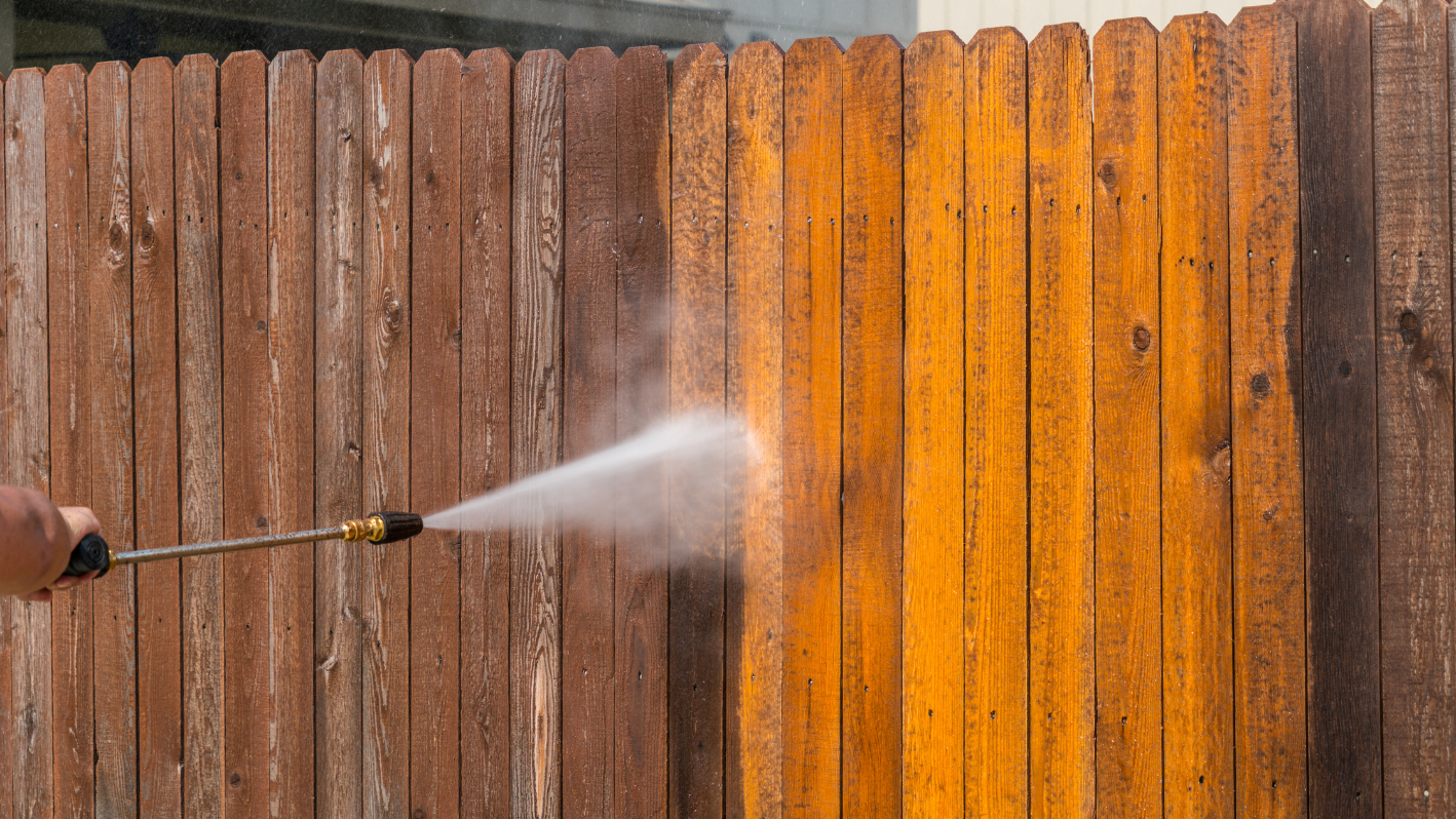 A person spraying water on a wooden fence